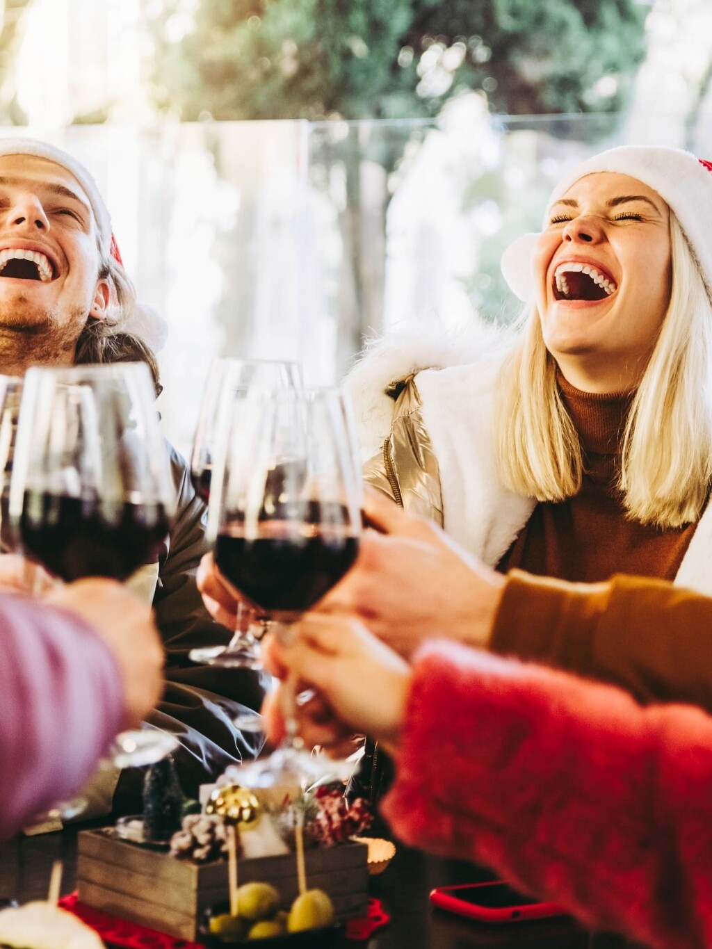 Group of friends laughing at Christmas party holding wine glasses