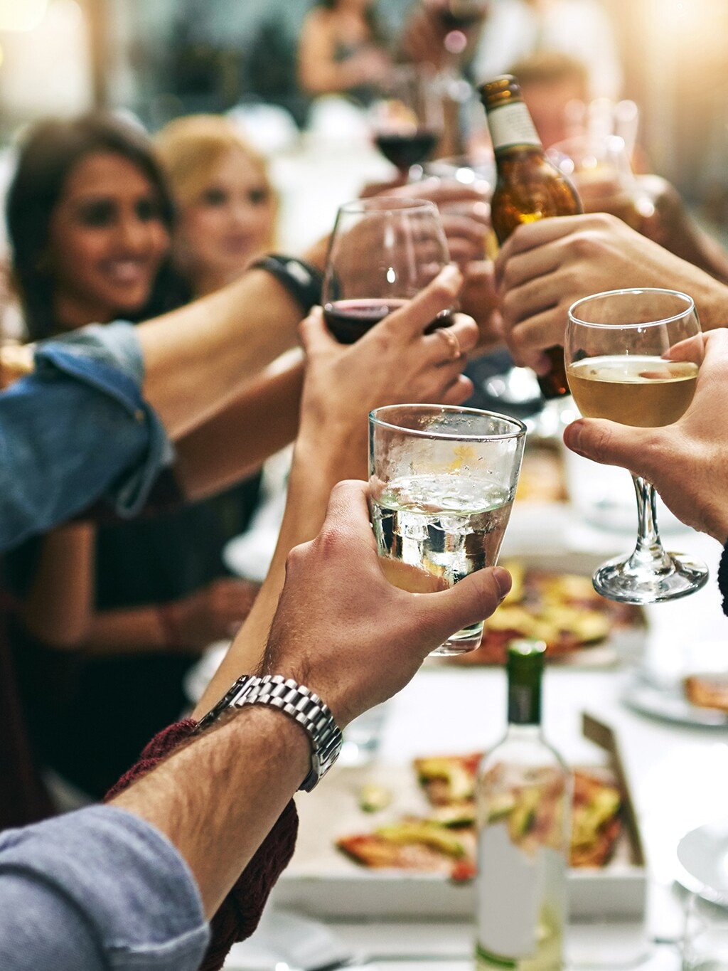 Group of women and men cheers at dinner party with cocktails